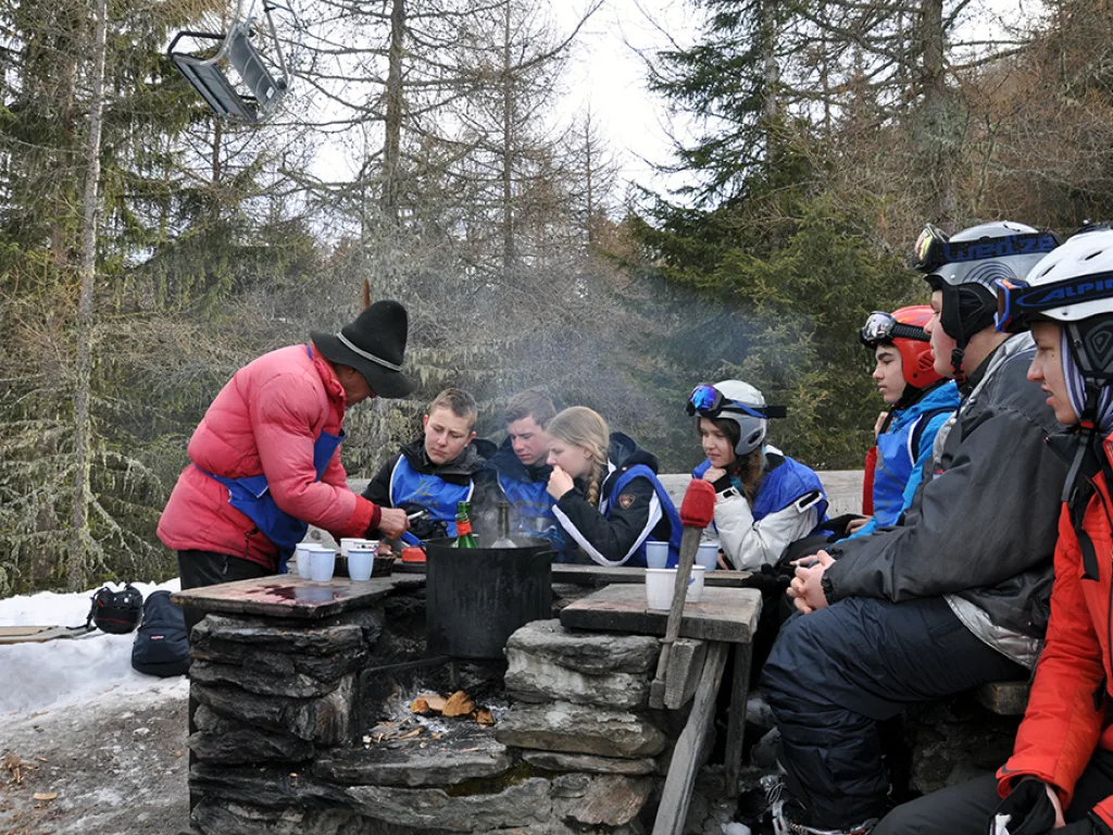 Gruppe steht um eine Feuerstelle vor der Hütte.